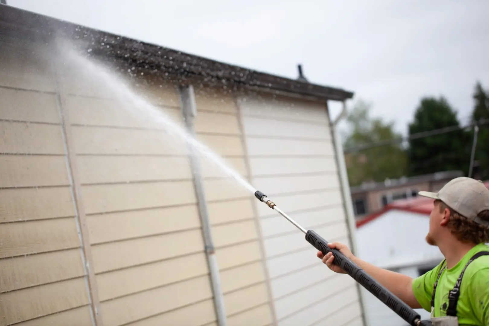 Person using a pressure washer to clean a house exterior.