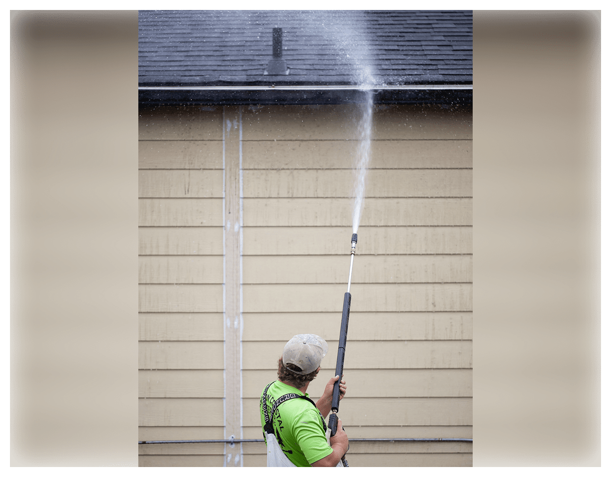Person power washing a building's exterior wall.