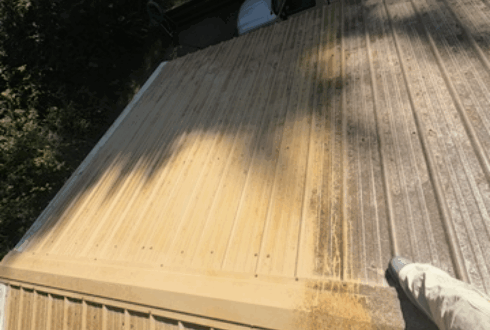 A wooden deck being pressure washed, showing a clear contrast between cleaned and dirty areas.