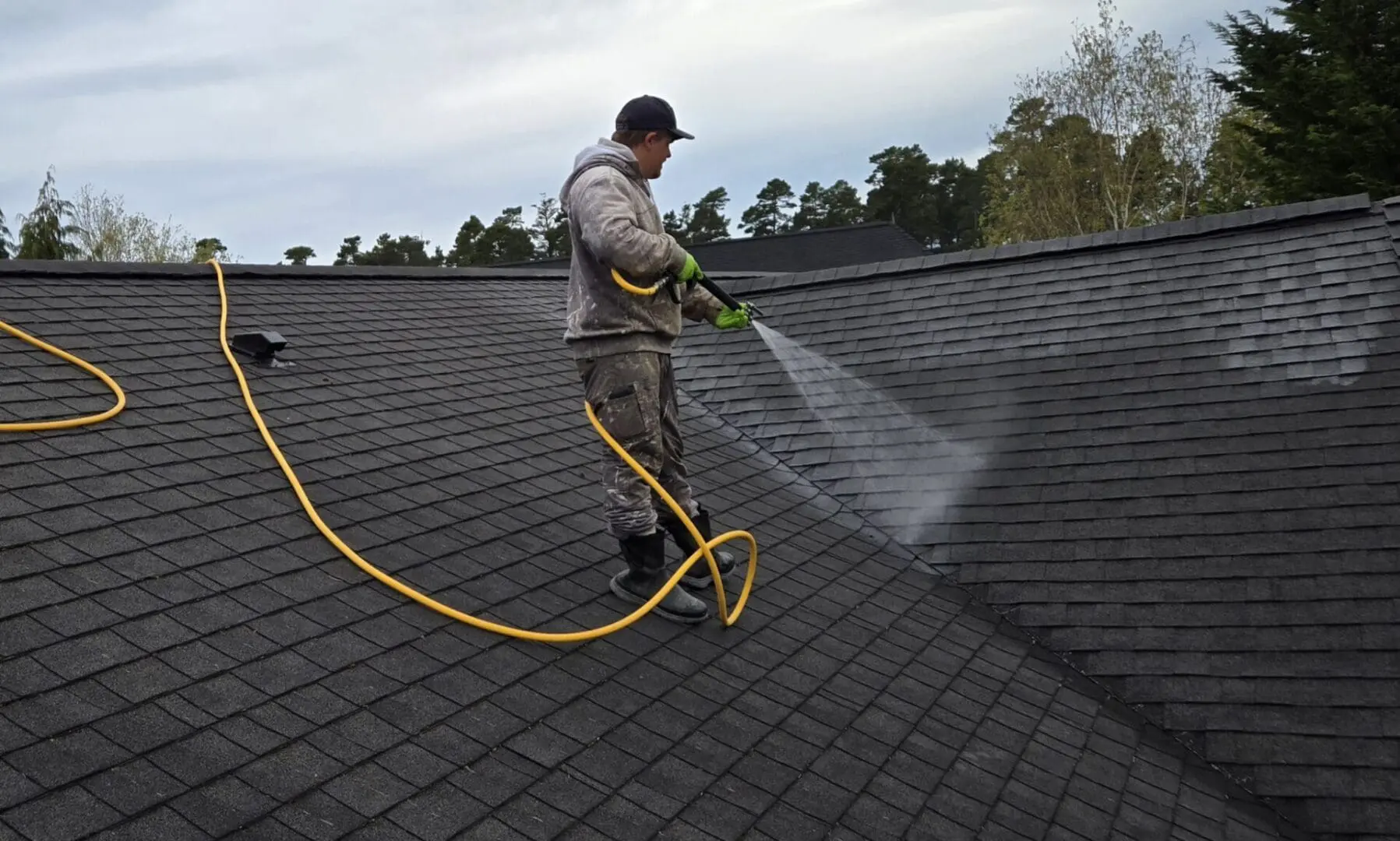 Worker pressure-washing asphalt shingle roof